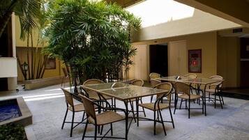 Zona d'interior amb terrassa, taules i cadires, envoltada de plantes i una petita piscina.
