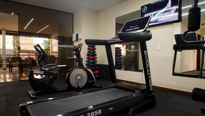 A gym with a treadmill, exercise bikes, and a TV screen. - Cedro Hotel (Londrina)