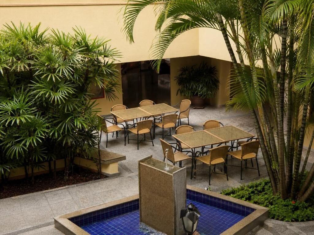 An outdoor patio area with tables and chairs, surrounded by greenery and a small pool.