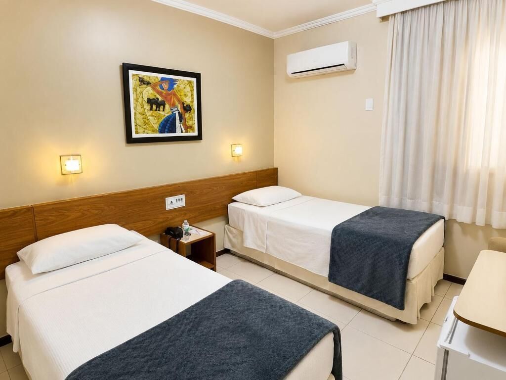 A hotel room with two beds, a nightstand, a wall-mounted air conditioner, and a painting on the wall.