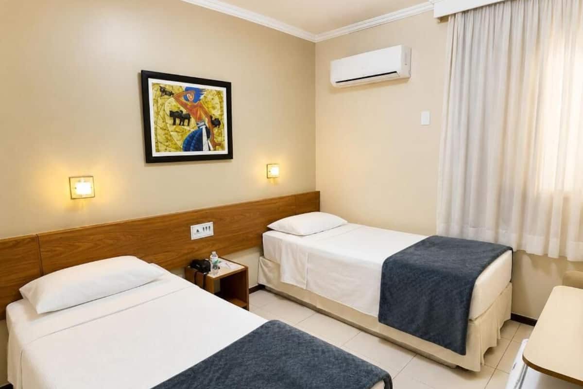 Una habitación de hotel con dos camas, una mesita de noche, aire acondicionado de pared y un cuadro en la pared.