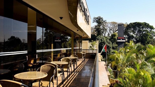 A hotel with outdoor seating, a flag, and lush greenery. - Cedro Hotel (Londrina)