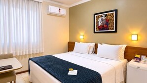 A hotel room with a bed, bedside tables, a desk, and a window with curtains. - Cedro Hotel (Londrina)