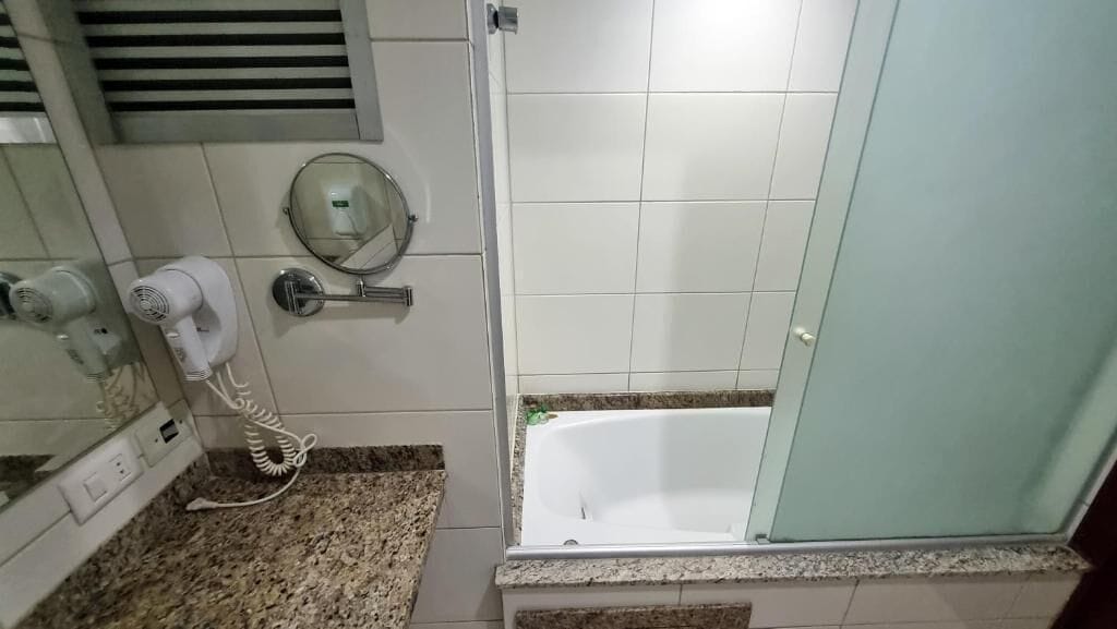 A bathroom with a white bathtub, a hairdryer, and a mirror.