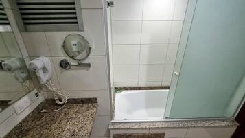 A bathroom with a white bathtub, a hairdryer, and a mirror.
