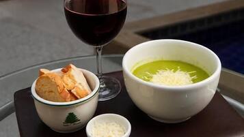 Une table à manger avec un verre de vin rouge, un bol de soupe, un assortiment de fromages et une petite assiette de pain.