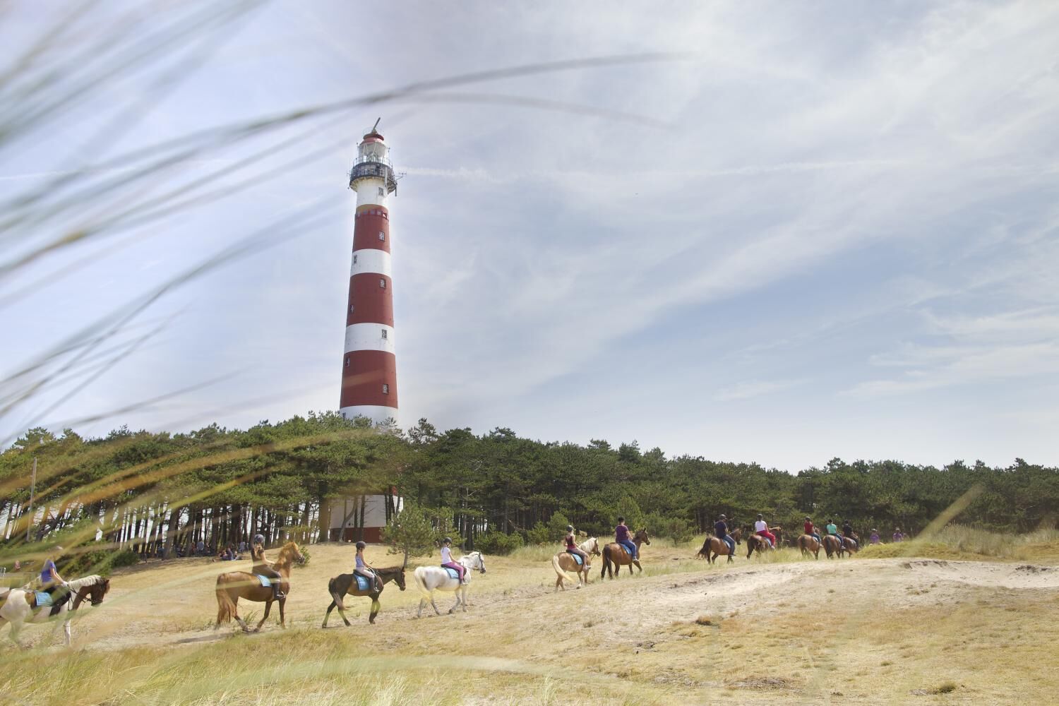 A lighthouse on a hill with a group of people riding horses in the foreground.