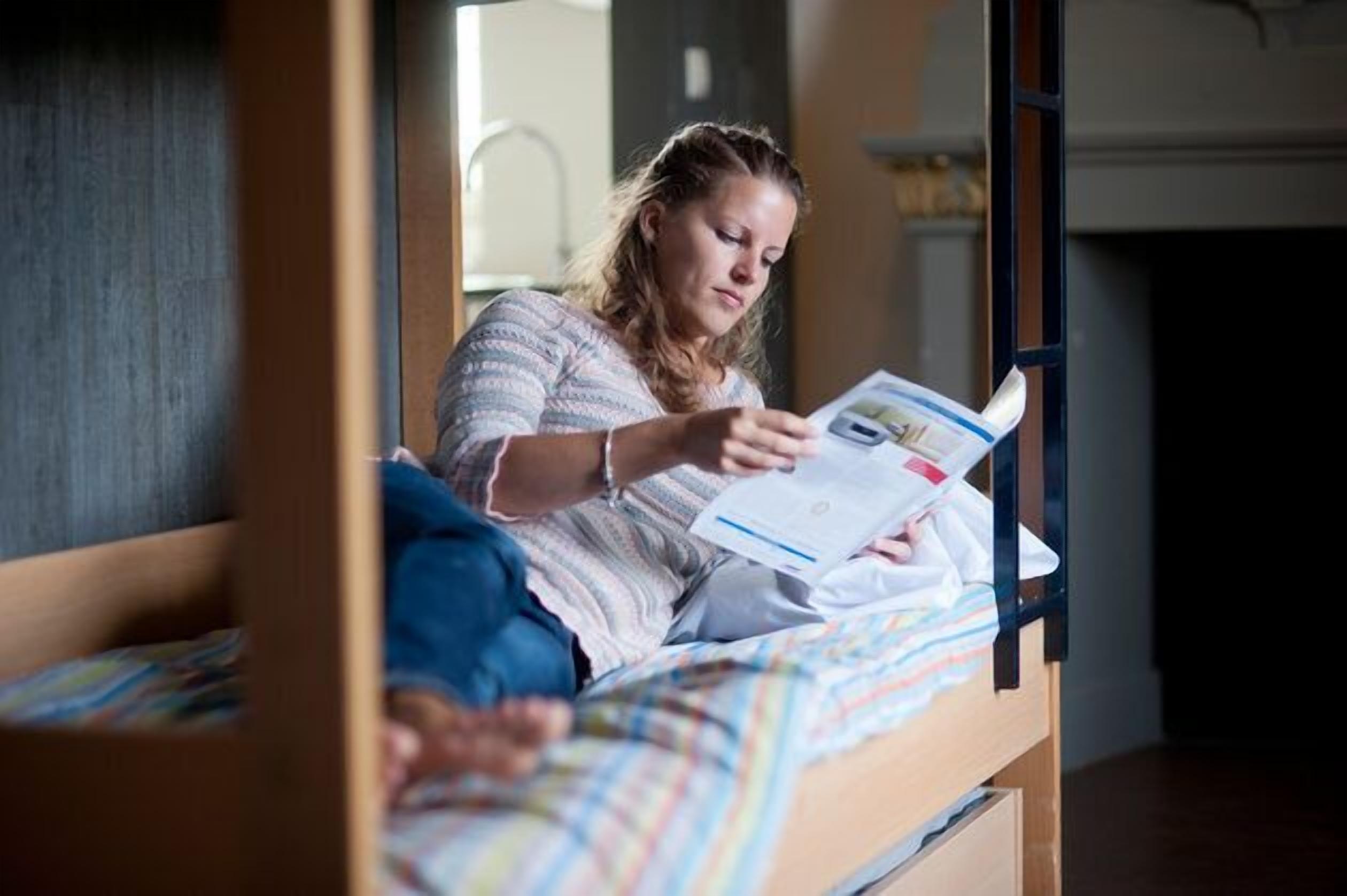 A person sitting on a bunk bed reading a book.