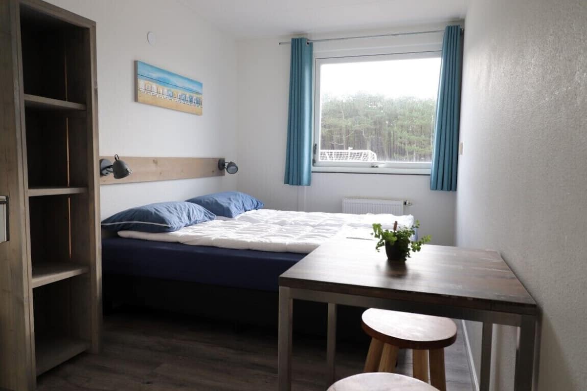 A small, tidy room with a single bed, a wooden table, and a window with curtains.