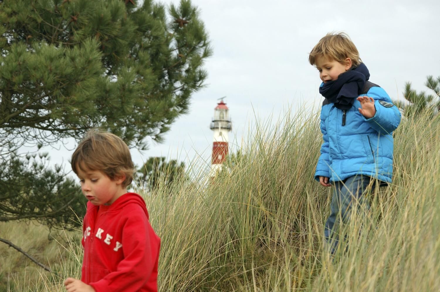 Dos infants jugant en un prat f alt amb un far al fons.