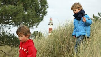 Dos infants jugant en un prat f alt amb un far al fons.