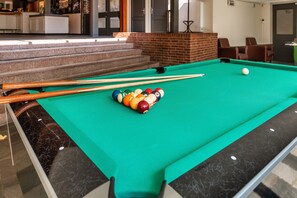 Une table de billard avec des billes et des queues, un mur en briques et un escalier menant à une pièce.