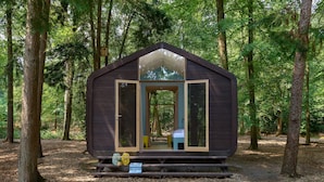 Une petite cabane avec un toit en pente, une porte d’entrée et un banc à l’extérieur.