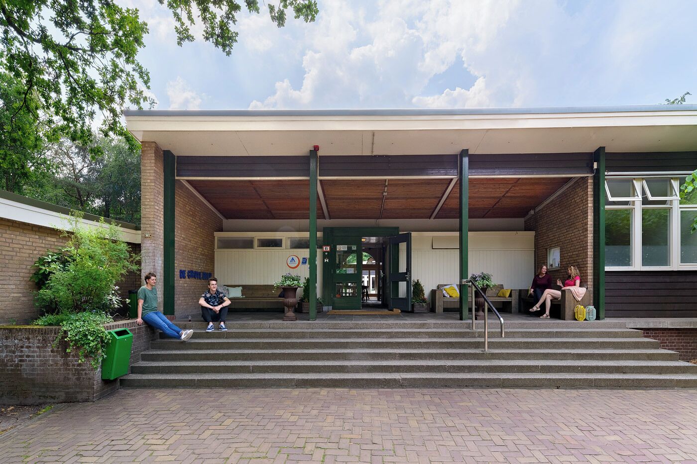 A building with a covered entrance, steps leading up to it, and a brick wall on one side.