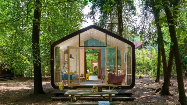 Une cabane avec un dôme de verre, située dans une forêt, et dotée d’une table et de chaises à l’extérieur, idéales pour un pique-nique.