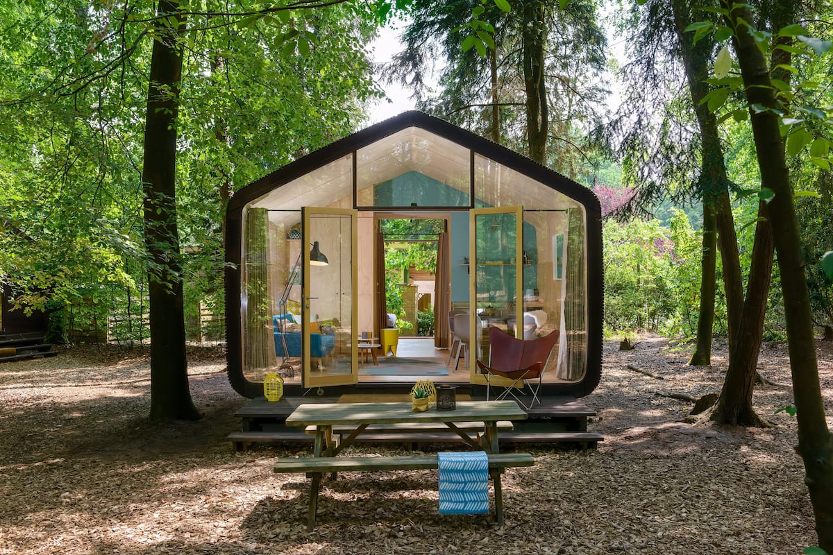 Eine glaskuppelartige Hütte im Wald mit einem Picknicktisch und Stühlen davor.