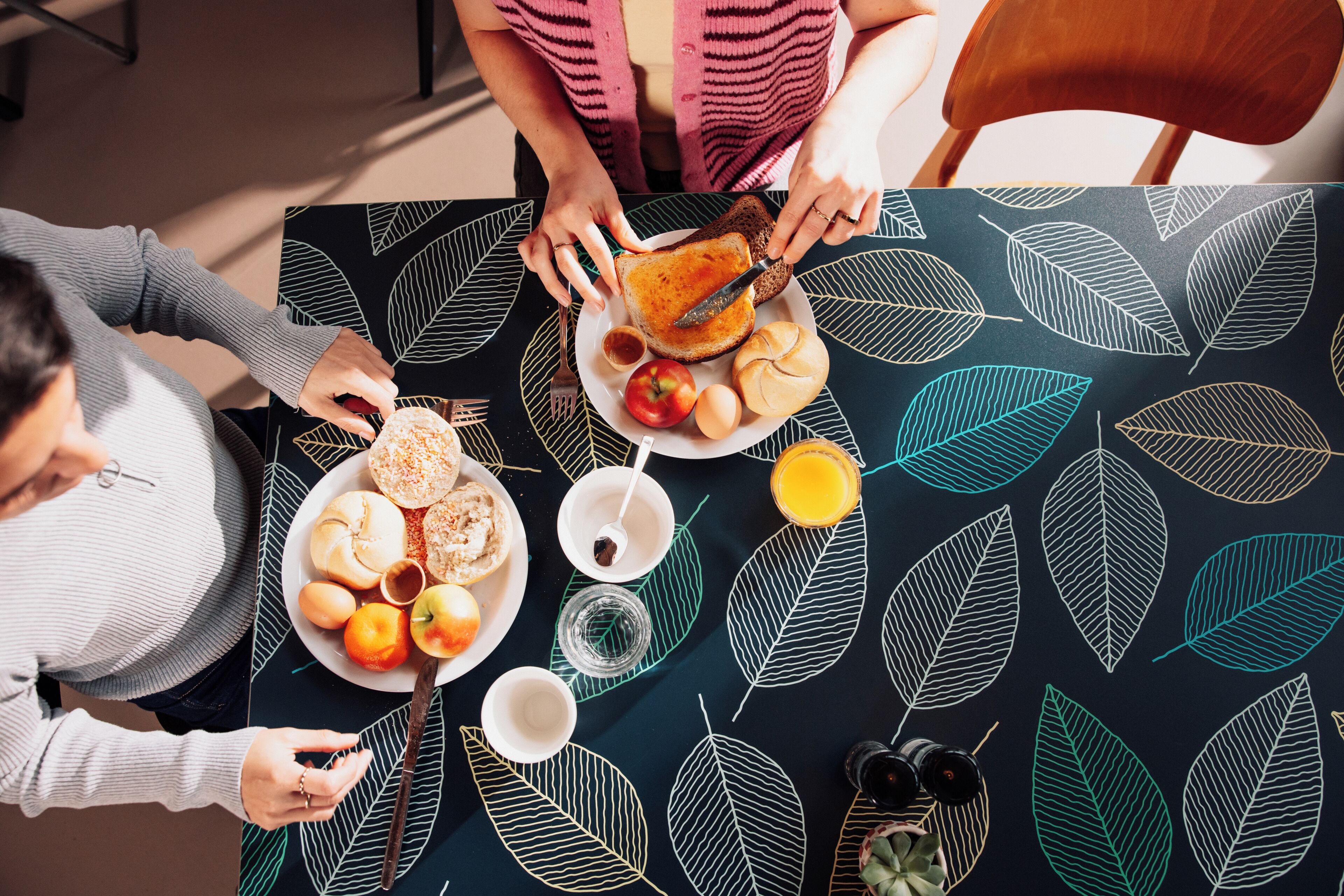 Una mesa de comedor con mantel estampado con motivos de hojas, un plato de comida y un vaso de jugo.