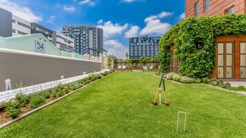 A well-maintained lawn with a croquet set, surrounded by buildings and a clear sky.
