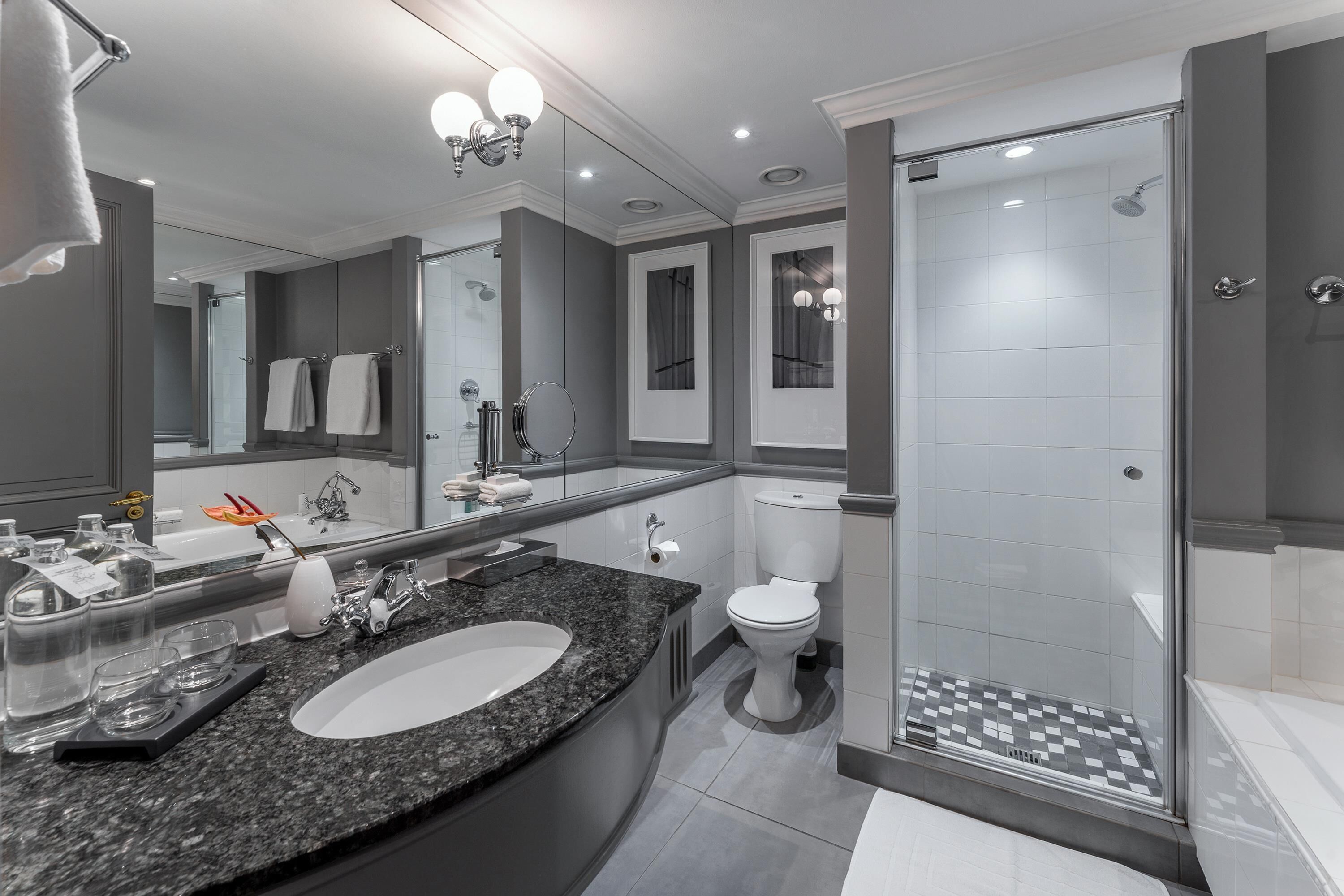 A modern bathroom with a large mirror, a sink, a toilet, and a walk-in shower.