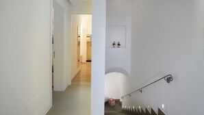 A modern interior with a staircase, a hallway leading to a room, and a small wall-mounted shelf with two figurines. - Santacroce Luxury Rooms (Lecce)
