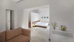 A modern hotel room with a bed, a sofa, a nightstand, and a wall-mounted air conditioning unit. - Santacroce Luxury Rooms (Lecce)