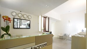 A reception area with a reception desk, clocks, and a seating area with chairs and tables. - Santacroce Luxury Rooms (Lecce)