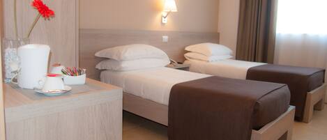 Una habitación de hotel con dos camas, una mesita de noche con lámpara, un florero con flores y una cafetera.