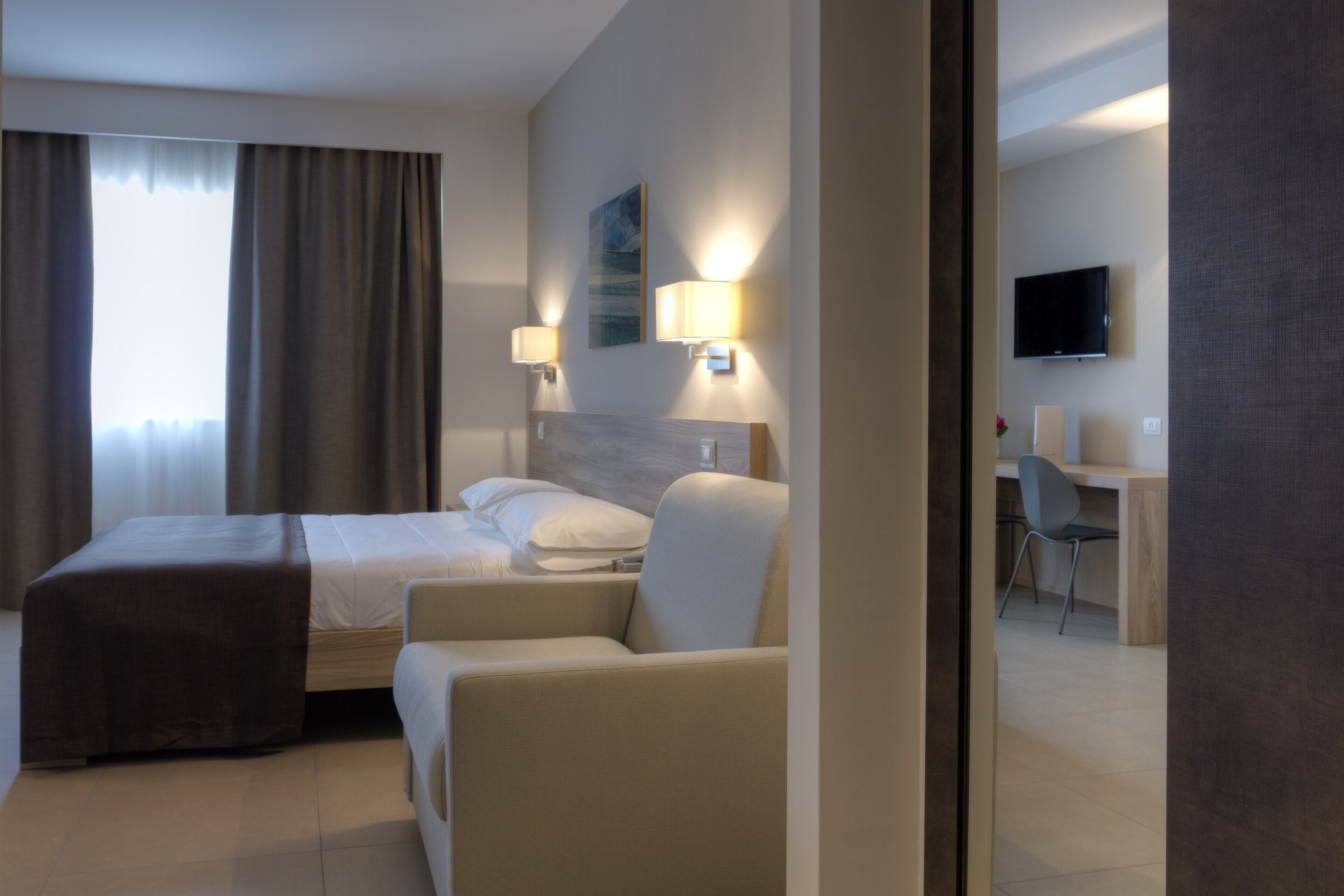 Een moderne hotelkamer met een bed, twee bedlampen, een bureau met stoel, en een televisie aan de muur.