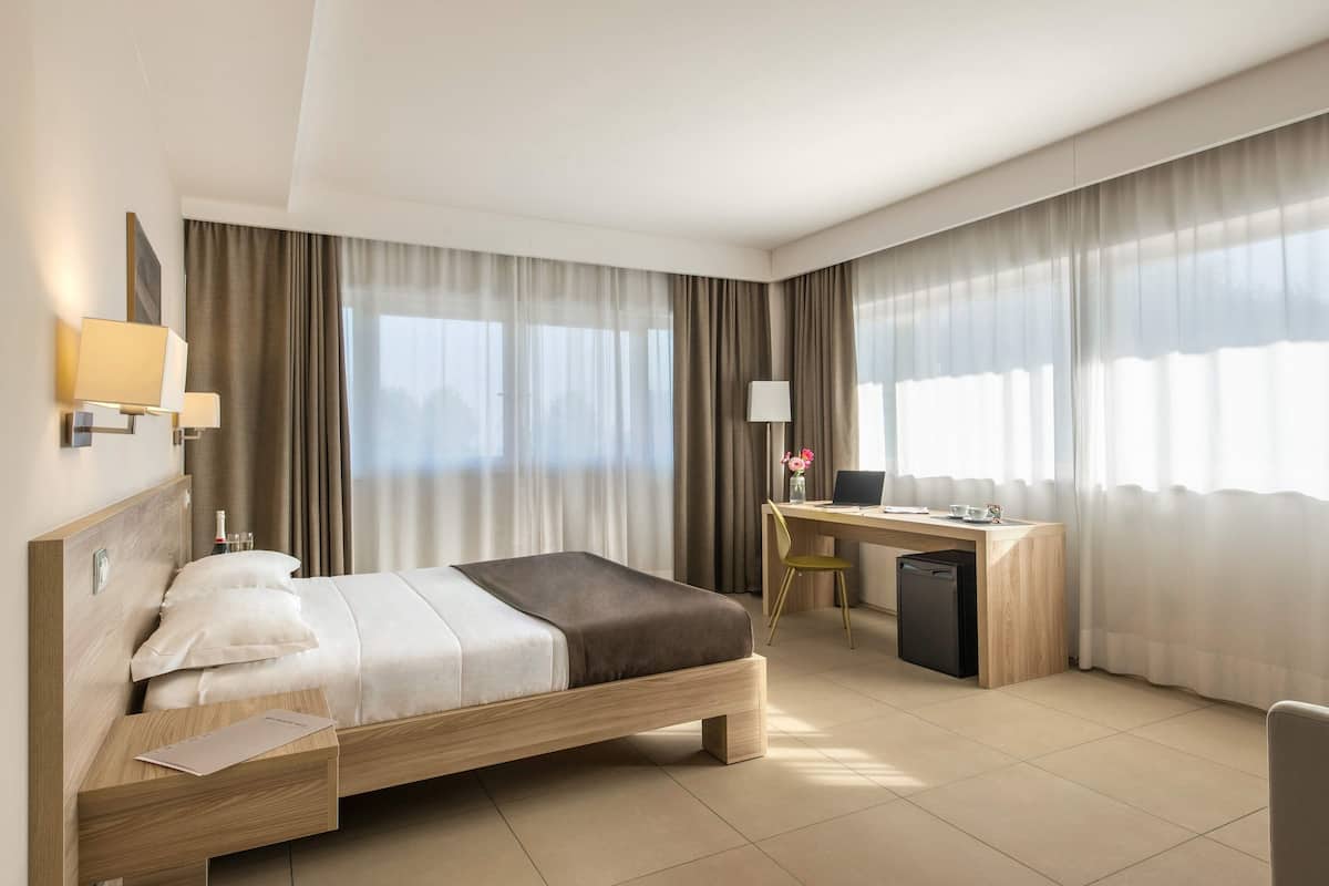 Ein modernes Hotelzimmer mit einem hölzernen Bett, einem Schreibtisch, einem Stuhl und einem kleinen Kühlschrank.