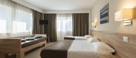 A hotel room with a large bed, a smaller bed, a sofa, a TV, and a bedside table with a book.