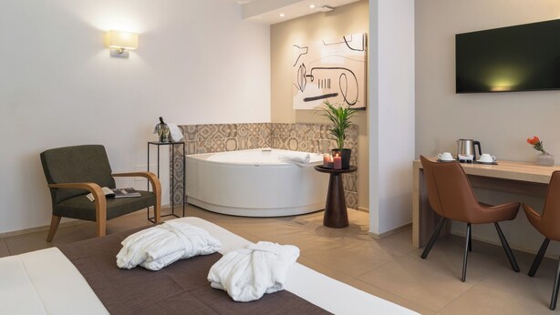 Habitación de hotel moderna con una bañera redonda, un escritorio con dos sillas, un televisor de pantalla plana y una planta en maceta.