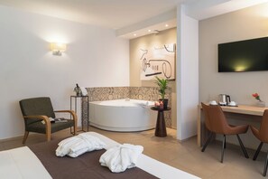 Habitación de hotel moderna con una bañera redonda, un escritorio con dos sillas, un televisor de pantalla plana y una planta en maceta.