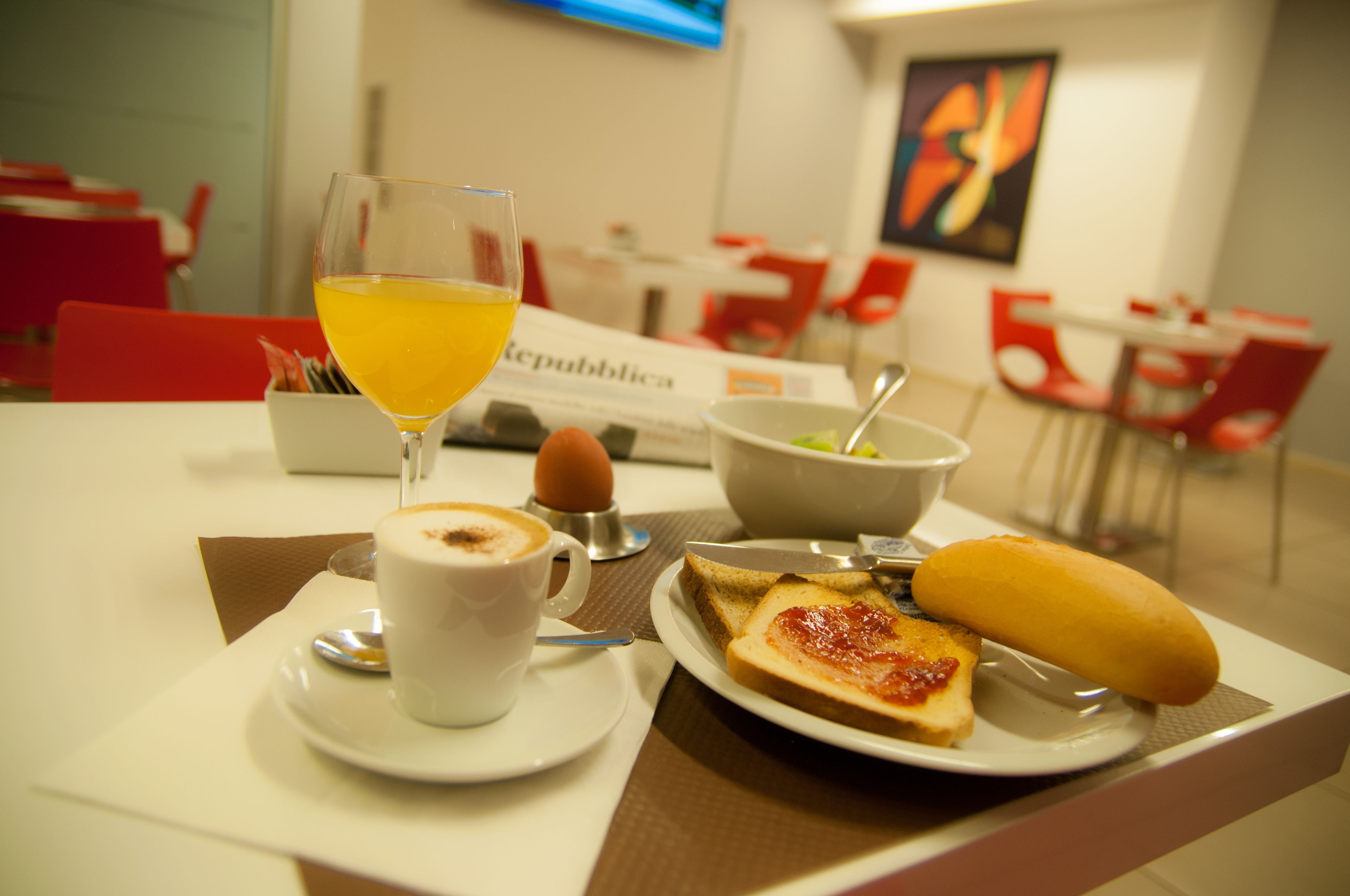 Une table mise pour le petit-déjeuner avec une tasse de café, un verre de jus d’orange, des tartines à la confiture et un bol de salade.