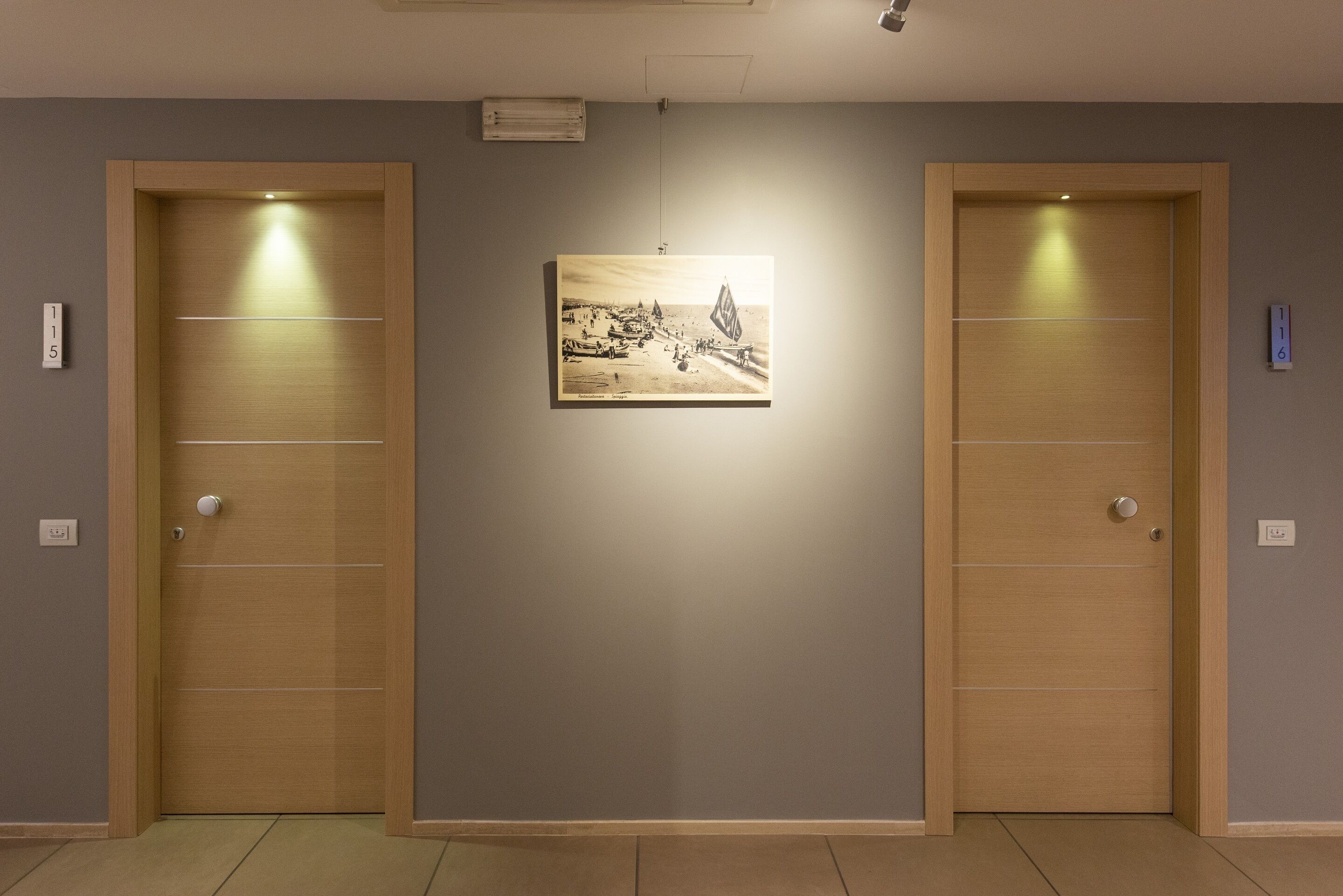 A hallway with two wooden doors, a framed picture on the wall, and a light fixture above.