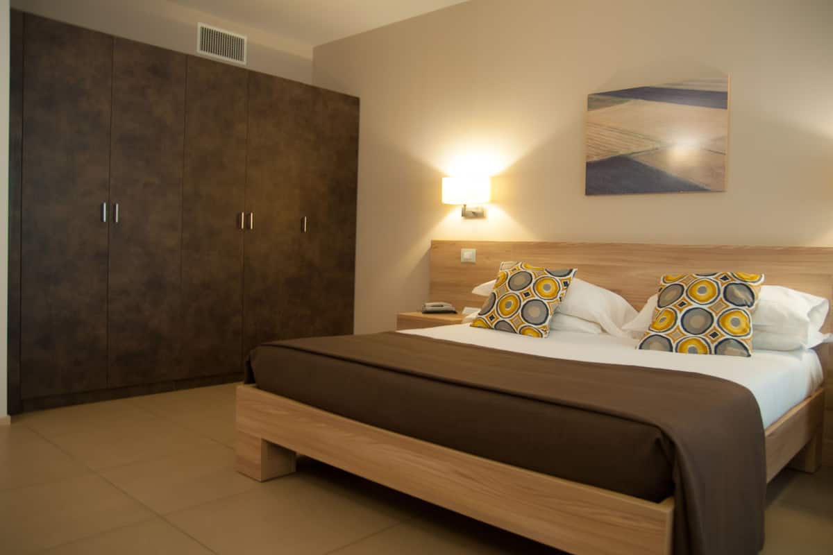Ein Schlafzimmer mit großem Kleiderschrank, einem Bett mit gemusterten Kissen und einer Wandlampe.