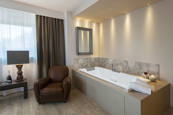 A modern bathroom with a large bathtub, a chair, a table with a lamp, and a mirror. - Hotel Dimorae Rooms and Suites - Apartments (Civitanova Marche)