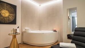 Un baño moderno con una bañera independiente, una mesa redonda con base dorada y un sillón de masaje negro.