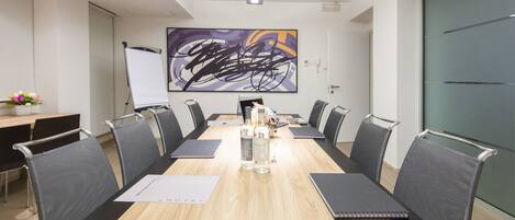 A conference room with a long table, black chairs, a whiteboard, and a large abstract painting on the wall.
