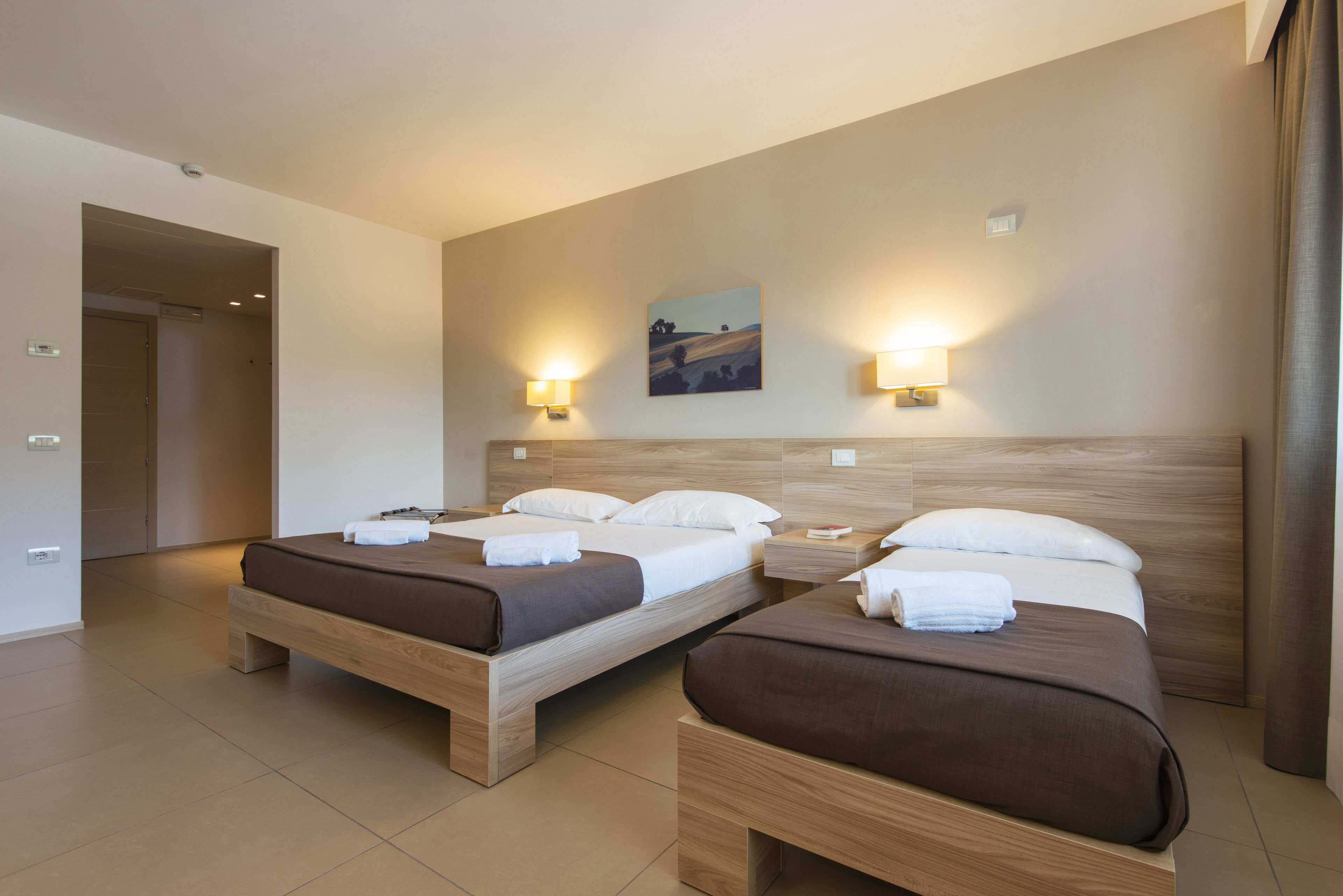 A hotel room with two beds, a painting on the wall, and two wall-mounted lamps.