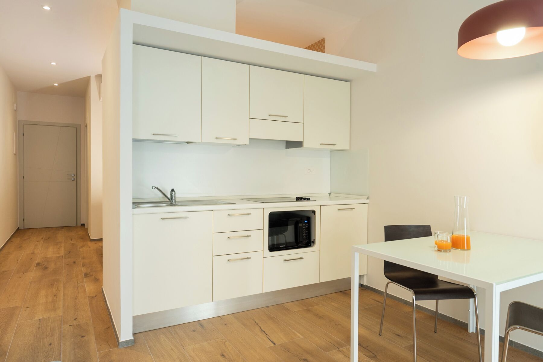 A modern kitchen with white cabinets, a built-in oven, and a dining area with a table and chairs.