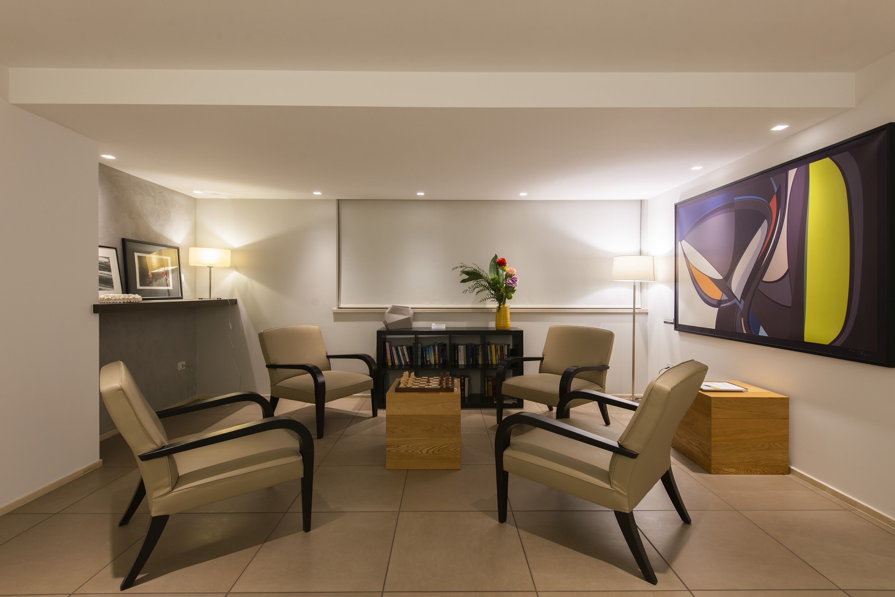 A modern conference room with a round table, four chairs, a bookshelf, and a large abstract painting on the wall.
