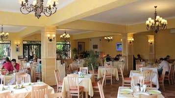 A restaurant with multiple tables and chairs, chandeliers, and a view of the outdoors.