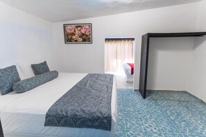 A bedroom with a bed, pillows, a painting, a window with curtains, and a blue patterned floor.