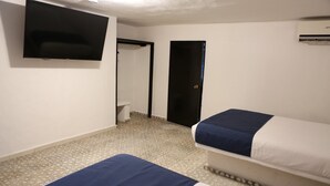 Ein Hotelzimmer mit zwei Betten, einem Fernseher, einer Tür und einer Klimaanlage.