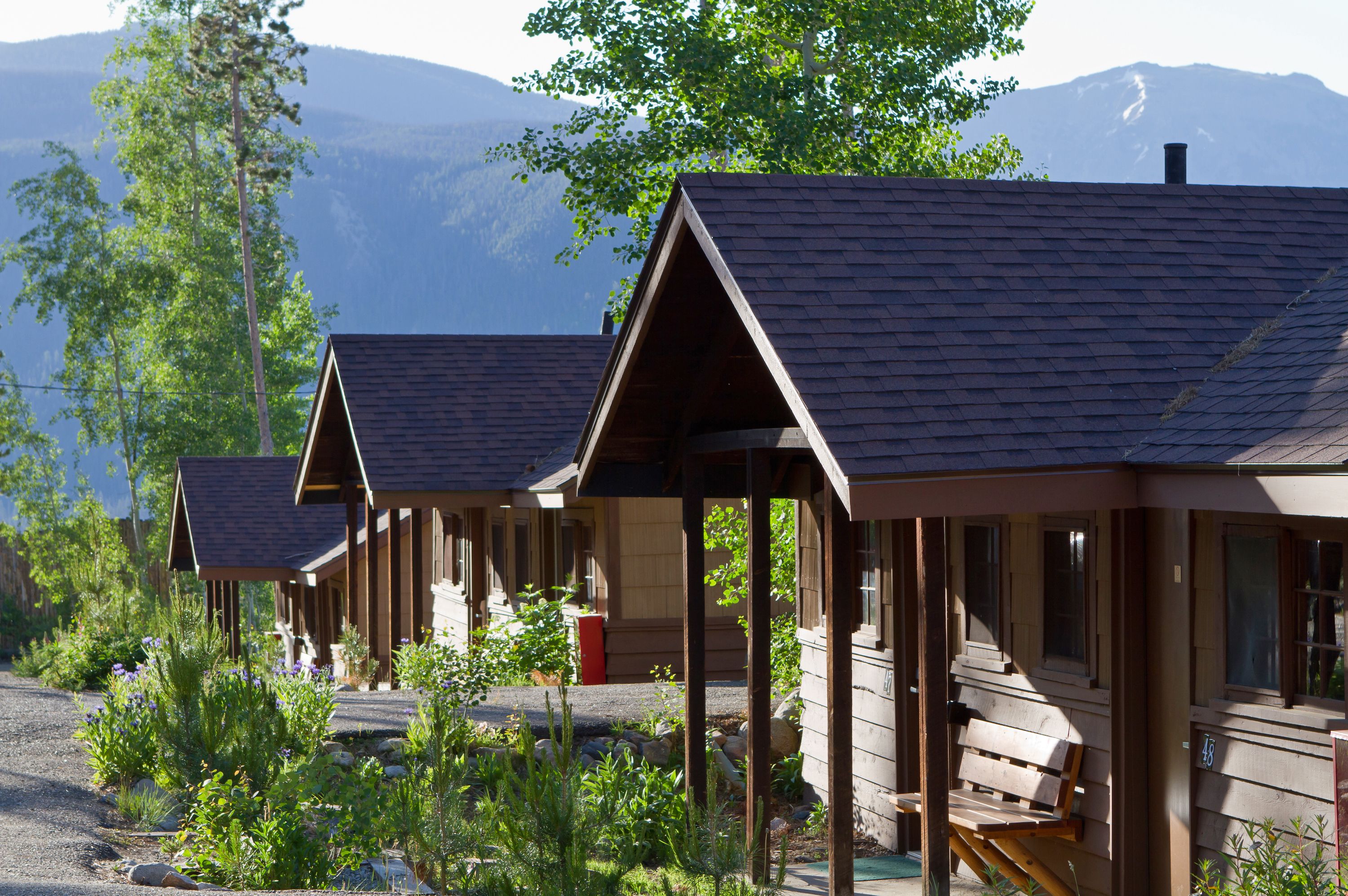A row of wooden cabins with pitched roofs, set against a backdrop of mountains.