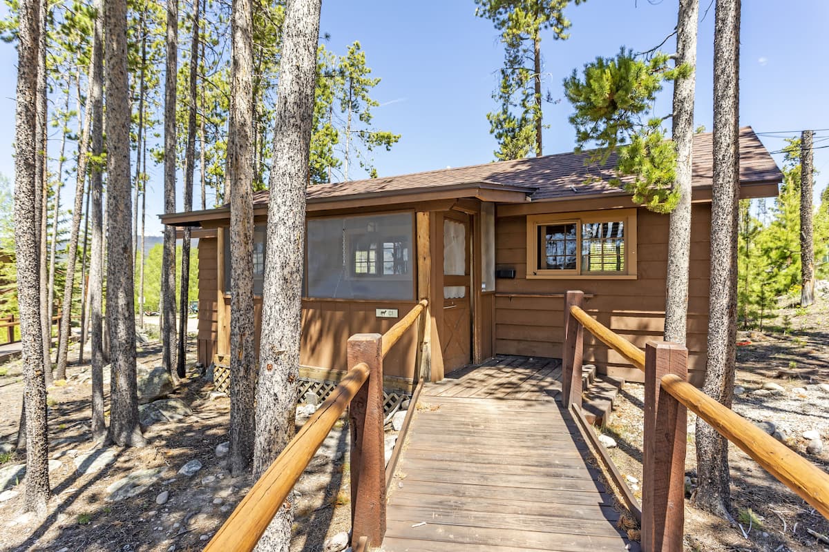Une cabane en bois dotée d’une terrasse et de balustrades, entourée de grands arbres.