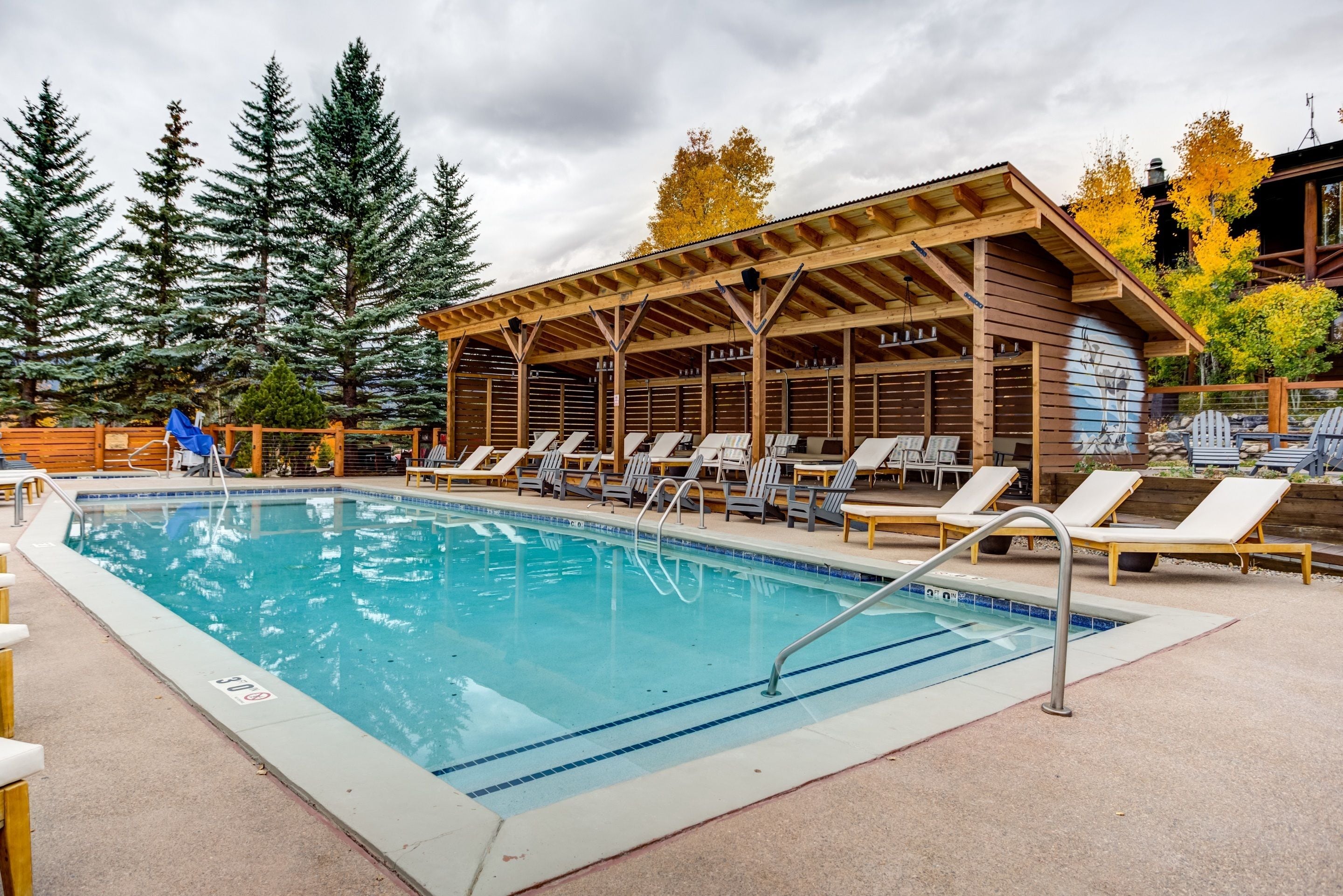 Un espace piscine avec des chaises longues, une terrasse en bois et un coin salon abrité.