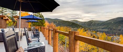 A wooden deck with outdoor seating and umbrellas, overlooking a mountainous landscape with autumn foliage.