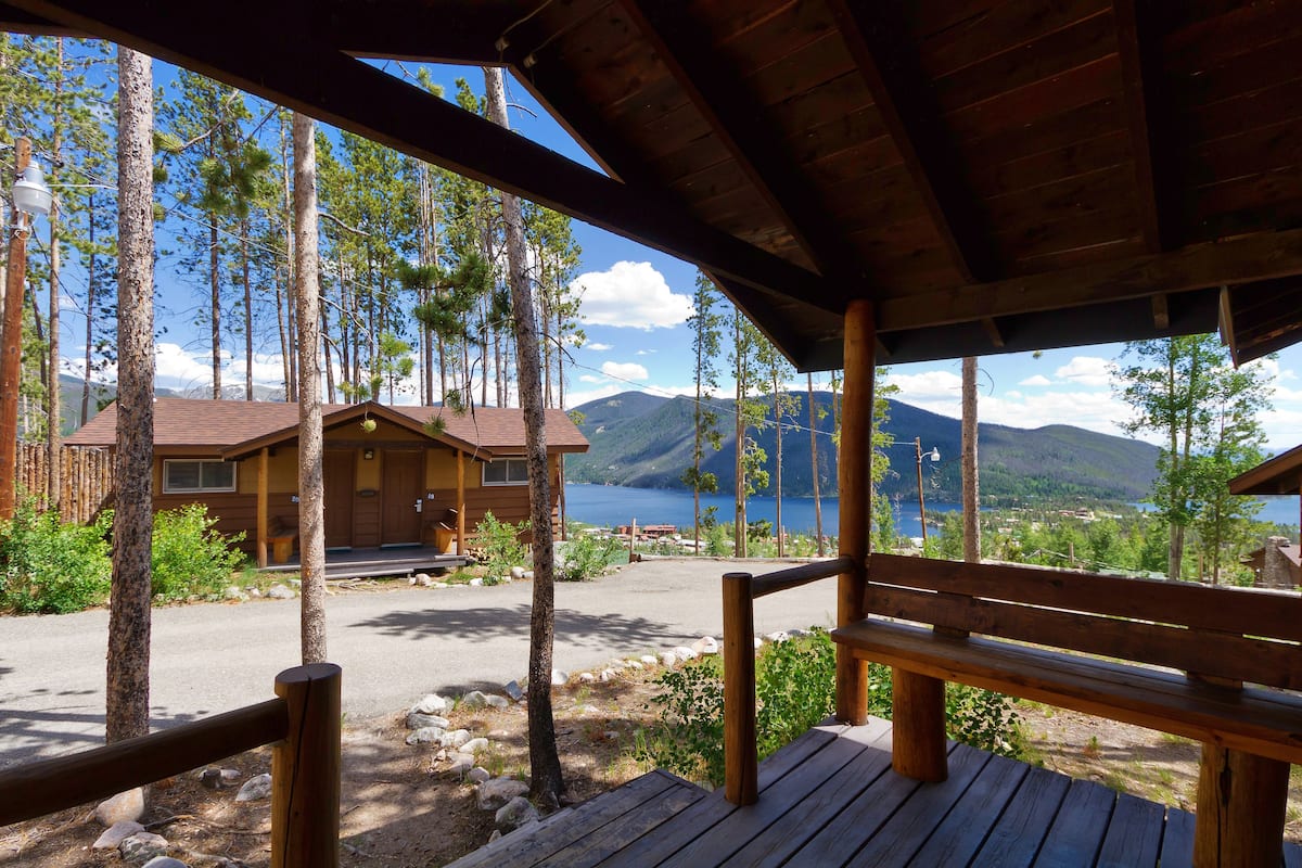 Une terrasse en bois avec un banc donnant sur un chalet et un lac.