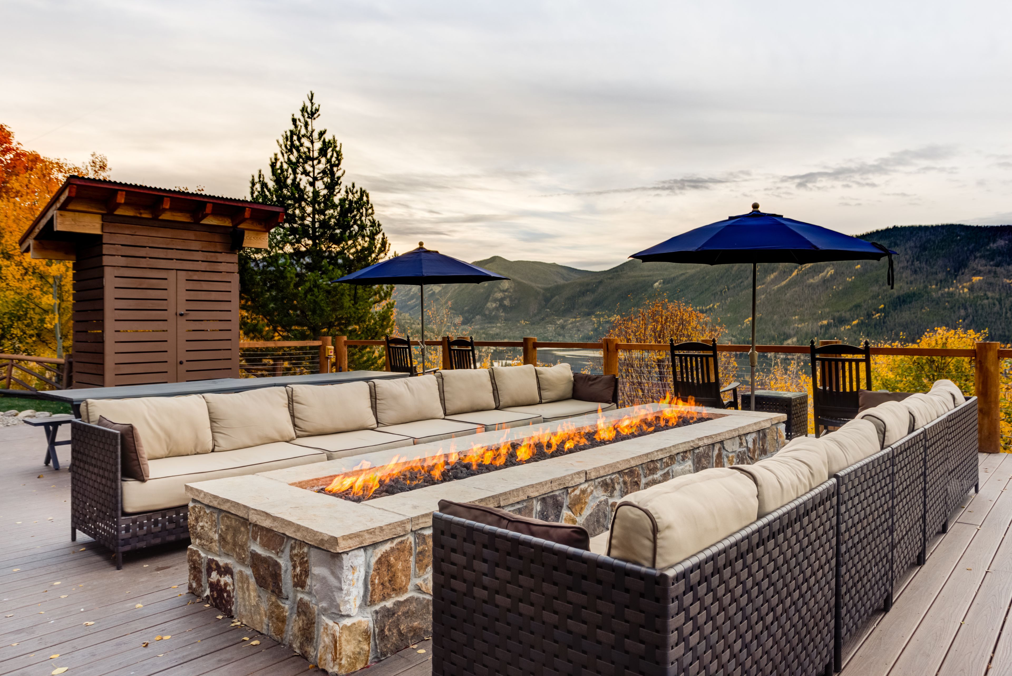 An outdoor deck with a stone fire feature, a long sofa, and two umbrellas.